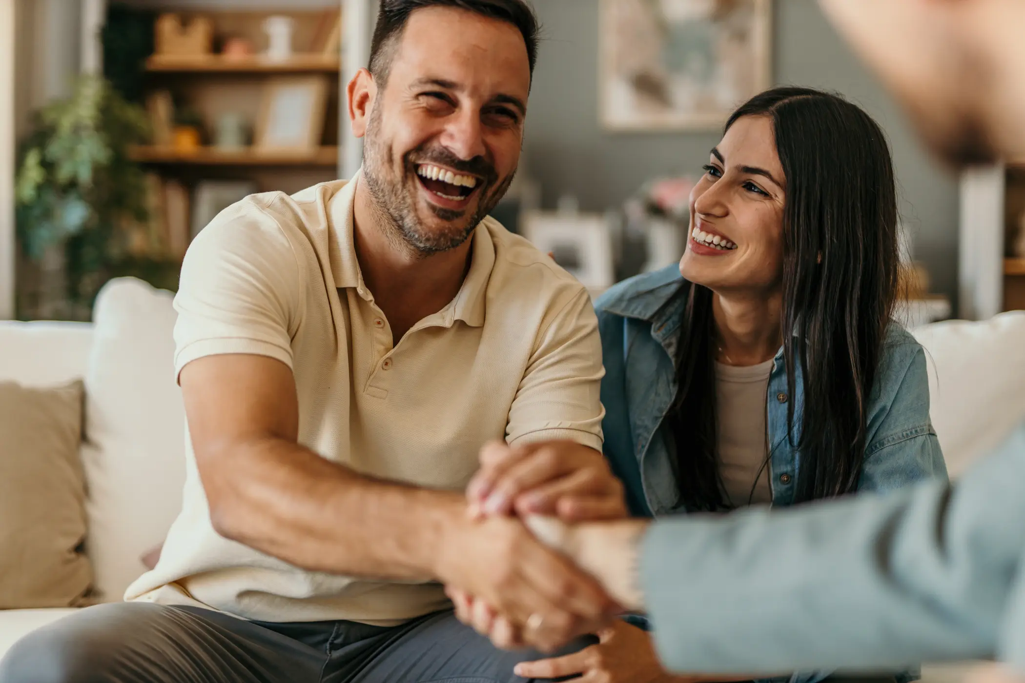 happy couple on couch in living room approaching middle age shakes hand with certified financial planner